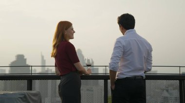 Şarabın neşe kaynağı yüksek bina manzarası günbatımı sıcak tonu ile gökyüzü, mutlu çift cam tutuyor, şarap neşe içinde şehir manzarası, şarap şehrin gökyüzü çatısı manzarası