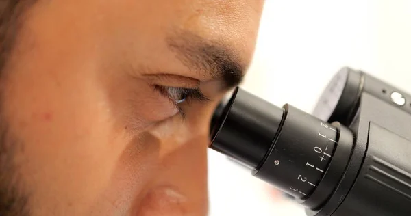 研究室で顕微鏡を通して見るプロの男性科学者の目を閉じます スマート科学は 医学科学のための研究を行っています 医学化学と生物学のラップの科学技術 — ストック写真