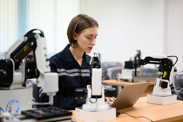 Female technician engineer using laptop checking and operating automatic robotic machine at industrial factory, Worker working with robotic system in factory