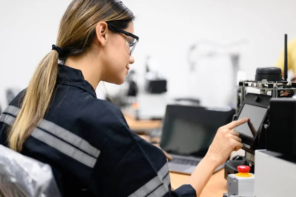 Female technician engineer using laptop checking and operating automatic robotic machine at industrial factory, Worker working with robotic system in factory