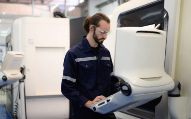 Profesyonel teknisyen endüstriyel fabrikada otomatik makinenin bir kısmını kontrol edip tamir ediyor.