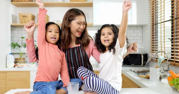 Happy family in kitchen, Duo girl rise hands up with mother cooking in kitchen, Family smiling together