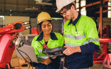 Happy male and female mechanical engineers in hard hat and safety uniform controlling machinery standing at manufacturing area of industrial factory