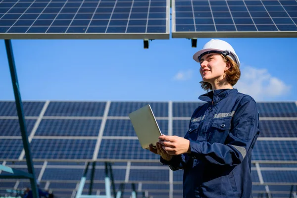 Female engineer holding laptop checking solar panels at industrial solar cell farm, Engineer working at power station, Electric system maintenance at solar panels field, Eco friendly and clean energy