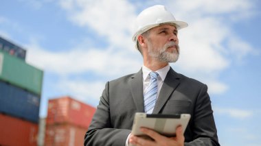Elinde tablet taşıyan siyah takım elbiseli akıllı işadamının portresi kargo istasyonunda çalışan profesyonel ustabaşı, depo mühendisi kontrol ve çalışma yapan