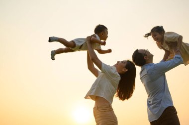 Anne ve baba, akşamları birlikte parkta oynayan çocukları, neşeli aile manzarasını, anne ve çocukları parkta pikniği, sağlıklı yaşam tarzını,