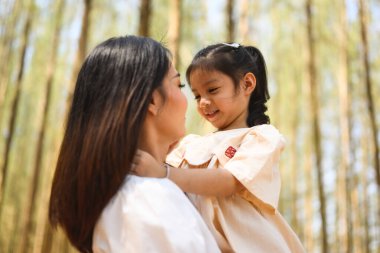 Anne, tatlı kızını kucağına alıp çam ormanlarında gülüyor, neşeli aile parkta piknik yapıyor, anne ve baba, kız ve oğluyla birlikte doğaya seyahat ediyor, sağlıklı bir aileye sahip.