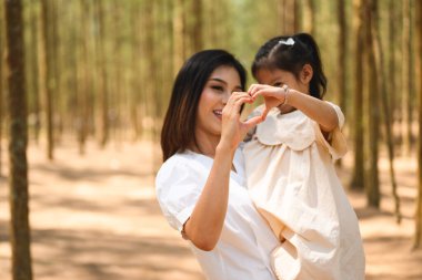 Anne, tatlı kızını kucağına alıp çam ormanlarında gülüyor, neşeli aile parkta piknik yapıyor, anne ve baba, kız ve oğluyla birlikte doğaya seyahat ediyor, sağlıklı bir aileye sahip.