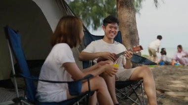 Mutlu Asyalı ebeveynler gitar çalıyor ve plaj kampında seyahat ediyor mutlu çok nesilli aile hafta sonları birlikte iyi vakit geçiriyor insanlar sahilde, tatilde ve seyahat konseptinde eğleniyor.