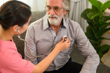 Steteskop hastası olan mutlu kadın doktor, evde ya da huzurevinde yaşlı bir hastaya bakan doktor ya da hemşire, ev ziyareti sırasında doktor ve yaşlı adam.