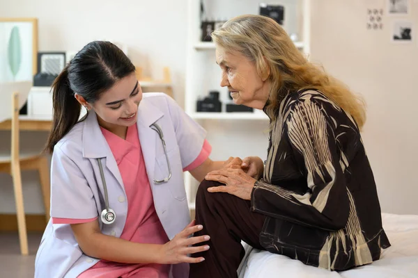 Happy doctor or nurse caregiver with senior patient at home or nursing home, Professional female doctor with stethoscope visiting patient, Doctor and senior woman during home visit