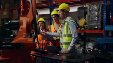 Bir grup teknisyen depoda robot makineleri kontrol ediyor ve onarıyor, endüstriyel imalat fabrikasında güvenlik üniforması koruması olan endüstri mühendisi çalışıyor.
