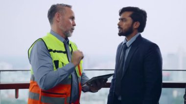 İnşaat mühendisi ustabaşı inşaat alanında iş adamıyla konuşuyor, gökdelen geçmişi ve yüksek inşaat alanı olan insanlar.