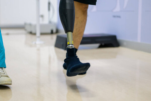 Физиотерапевт помогает пациенту с протезом ноги ходить между параллельными барами во время сеанса физиотерапии в больнице, новое производство искусственных конечностей для людей с ограниченными возможностями
