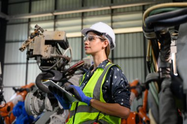 Endüstriyel fabrikada çalışan kendine güvenen kadın işyeri mühendisi, otomasyon teknolojisi fabrikasında robot makineleri kontrol eden kadın mühendis.