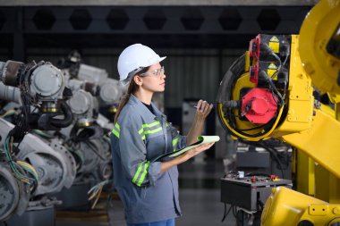 Fabrikada robot makine otomasyonuyla çalışan bakım mühendisi, endüstride akıllı teknolojili kadın teknisyen, robot makinenin parçalarını kontrol eden ve kontrol eden kadın işçi.