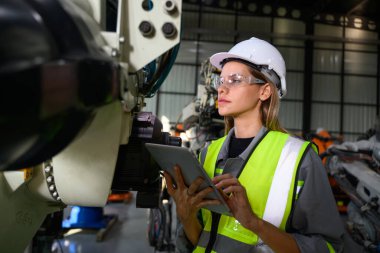Fabrikada robot makine otomasyonuyla çalışan bakım mühendisi, endüstride akıllı teknolojili kadın teknisyen, robot makinenin parçalarını kontrol eden ve kontrol eden kadın işçi.