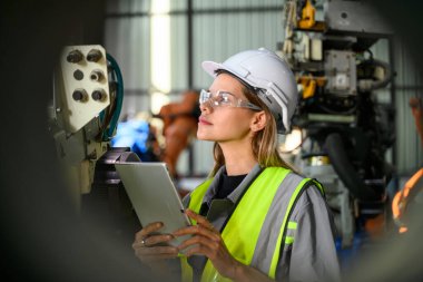 Fabrikada robot makine otomasyonuyla çalışan bakım mühendisi, endüstride akıllı teknolojili kadın teknisyen, robot makinenin parçalarını kontrol eden ve kontrol eden kadın işçi.