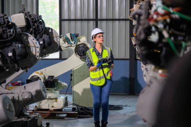 Endüstriyel fabrikada çalışan kendine güvenen kadın işyeri mühendisi, otomasyon teknolojisi fabrikasında robot makineleri kontrol eden kadın mühendis.