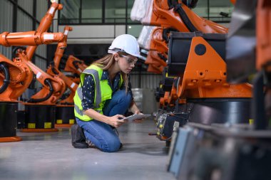 Endüstriyel fabrikada çalışan kendine güvenen kadın işyeri mühendisi, otomasyon teknolojisi fabrikasında robot makineleri kontrol eden kadın mühendis.