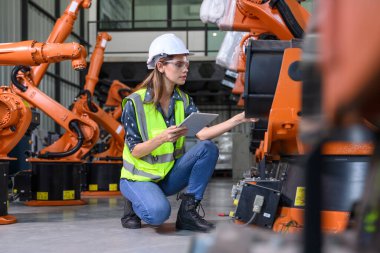 Endüstriyel fabrikada çalışan kendine güvenen kadın işyeri mühendisi, otomasyon teknolojisi fabrikasında robot makineleri kontrol eden kadın mühendis.
