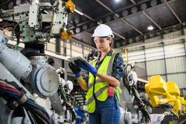 Endüstriyel fabrikada çalışan kendine güvenen kadın işyeri mühendisi, otomasyon teknolojisi fabrikasında robot makineleri kontrol eden kadın mühendis.