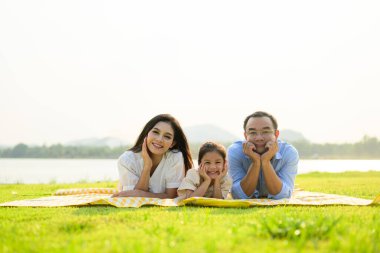 Mutlu bir aile hafta sonu parkta dinleniyor, baba ve kız parkta piknik yapıyor, ebeveynler kızlarıyla seyahat ediyor, mutlu bir aile hayatı sürüyor. 