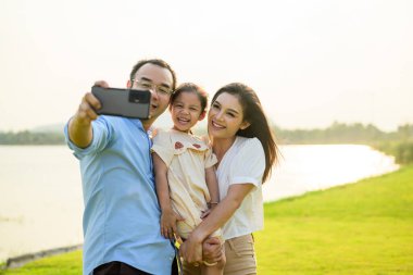 Mutlu bir aile hafta sonu parkta dinleniyor, baba ve kız parkta piknik yapıyor, ebeveynler kızlarıyla seyahat ediyor, mutlu bir aile hayatı sürüyor. 