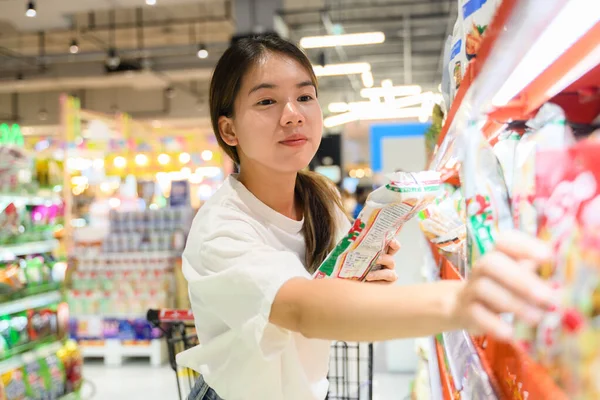 stock image Young woman using phone in grocery store and looking grocery list.