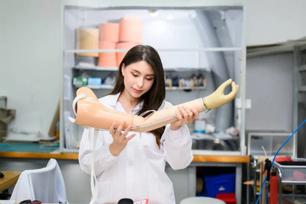 Female technician assembling and fixing parts of modern prosthetic arm, Prosthetic technician holding prosthetic device checking and controlling quality in laboratory, New artificial limb production