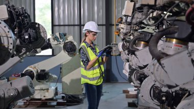 Endüstriyel fabrikada çalışan kendine güvenen kadın işyeri mühendisi, otomasyon teknolojisi fabrikasında robot makineleri kontrol eden kadın mühendis.