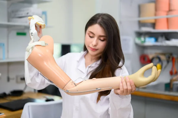 Female technician assembling and fixing parts of modern prosthetic arm, Prosthetic technician holding prosthetic device checking and controlling quality in laboratory, New artificial limb production