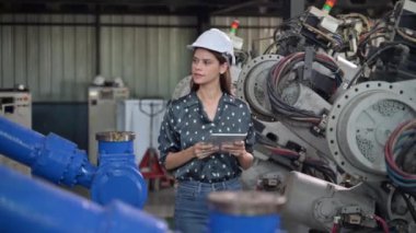 Endüstriyel fabrikada çalışan kendine güvenen kadın işyeri mühendisi, otomasyon teknolojisi fabrikasında robot makineleri kontrol eden kadın mühendis.