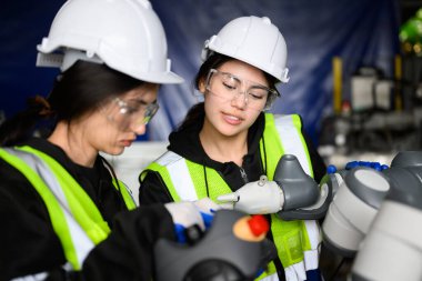 Couple of happy female maintenance engineers workers working with machine robotic arms at industrial factory, Technicians checking safety of machine maintenance, Industrial engineers with smart clipart