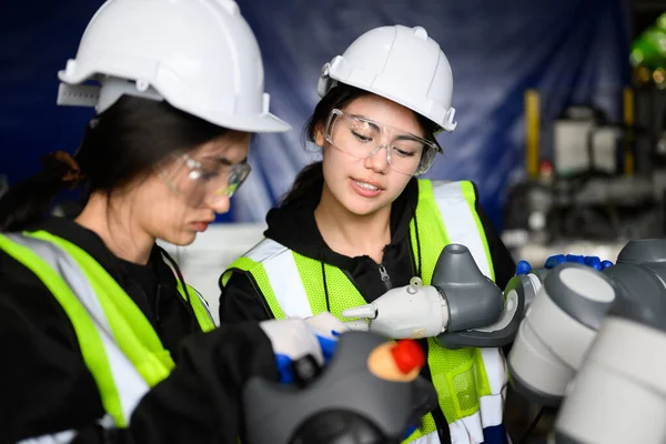 Couple of happy female maintenance engineers workers working with machine robotic arms at industrial factory, Technicians checking safety of machine maintenance, Industrial engineers with smart