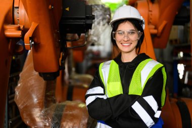 Endüstriyel fabrikada makineli robotik silahlarla çalışan kadın mühendis, endüstriyel yapı deposunda otomatik makineleri kontrol eden ve kontrol eden mühendis.