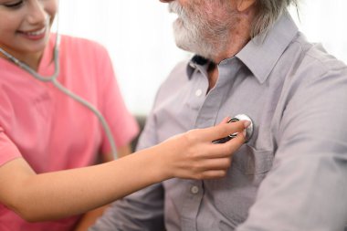 Steteskop hastası olan profesyonel kadın doktor, evde ya da huzurevinde yaşlı bir hastaya bakan doktor ya da hemşire, ev ziyareti sırasında doktor ve yaşlı adam.