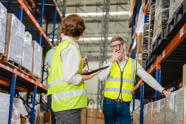 Professional warehouse workers with safety vest talking together checking goods in storage, Workers checking and controlling goods working in store factory, Warehouse worker with teamwork concept