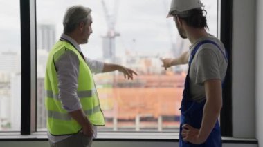 Yeni inşaat sahasında genç erkek elektrikçiyle birlikte çalışan kıdemli mühendis müteahhiti inşaat, mimarlık ve inşaat konseptinde birlikte çalışan iki teknisyen.