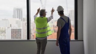 Yeni inşaat sahasında genç erkek elektrikçiyle birlikte çalışan kıdemli mühendis müteahhiti inşaat, mimarlık ve inşaat konseptinde birlikte çalışan iki teknisyen.