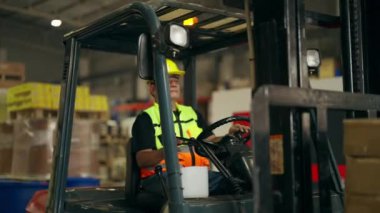 Fabrikada forklift üzerinde çalışan depo işçisi, sarı miğfer takan forklift şoförü, depoda çalışan forklift şoförü, endüstriyel mühendislik işçisi.