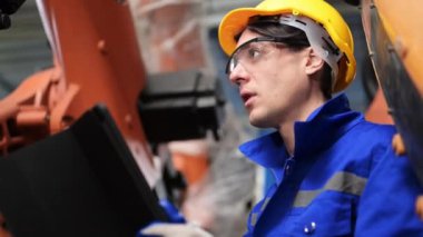 Endüstriyel fabrikada makine robotik silahlarıyla çalışan profesyonel mühendisler, makine ve bakım robotlarının güvenliğini kontrol eden teknisyenler, makineleri kontrol eden ve kontrol eden mühendisler,