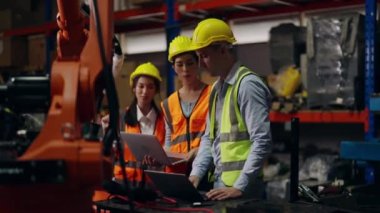 Bir grup teknisyen depoda robot makineleri kontrol ediyor ve onarıyor, endüstriyel imalat fabrikasında güvenlik üniforması koruması olan endüstri mühendisi çalışıyor.