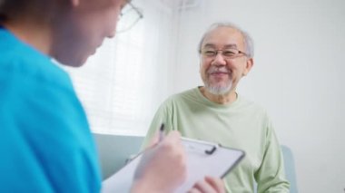 Young doctor examining senior patient at home visit, Senior man consulting medicine with pharmacist, Caregiver nurse taking care of elderly grandfather sitting on sofa at home, Medical service concept