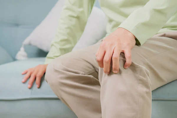 stock image Senior man using hand touching knee at pain point, Elderly man suffering from knee pain sitting on sofa at home, People with health problem concept