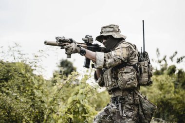 Korumalı savaş üniformalı asker, ormanda tüfekli asker, görevde asker, savaş meydanında saldırı tüfeğiyle ateş eden asker.