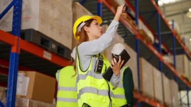 Mutluluk deposu mühendisleri çelik yelek giyiyorlar. Tablet kullanarak malzeme ve malzeme kontrol ediyorlar. Depo, Lojistik ve ticari ihracat konseptindeki ürün geçmişleri var.