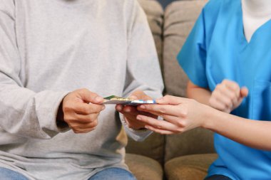 Young doctor examining senior patient at home visit, Senior man consulting medicine with pharmacist, Caregiver nurse taking care of elderly grandfather sitting on sofa at home, Medical service concept