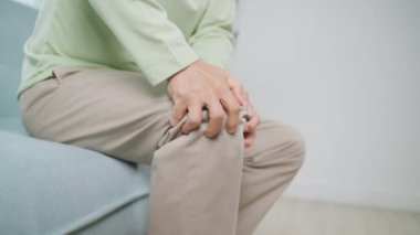 Senior man using hand touching knee at pain point, Elderly man suffering from knee pain sitting on sofa at home, People with health problem concept