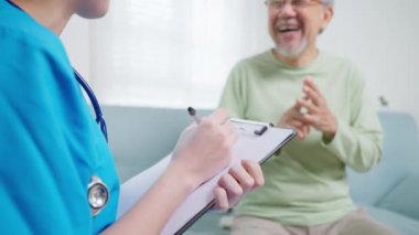 Young doctor examining senior patient at home visit, Senior man consulting medicine with pharmacist, Caregiver nurse taking care of elderly grandfather sitting on sofa at home, Medical service concept